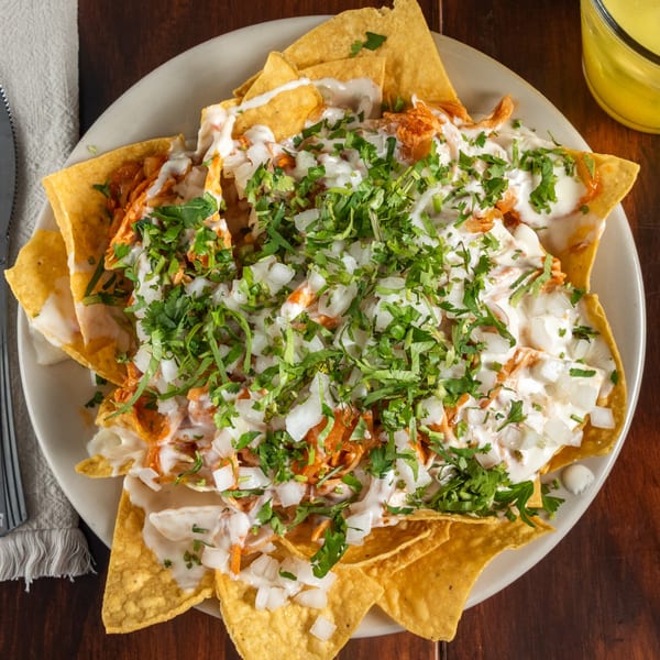 Tacos Godoy nachos with shredded chicken, white sauce, diced onions, and cilantro on a white plate.
