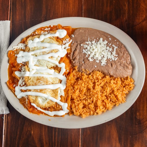 Chilaquiles with fried eggs, refried beans, and Mexican rice on a white plate.