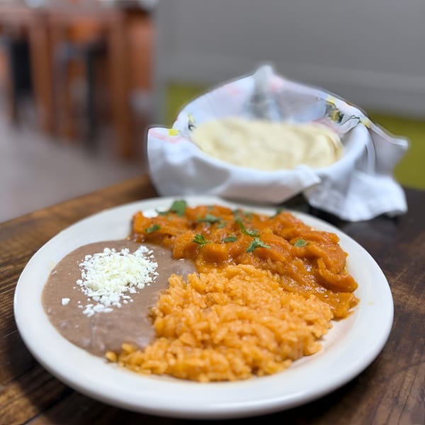 A Mexican plate with refried beans, rice, and stewed meat, with a basket of tortillas.