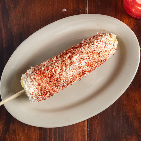 Elote, Mexican street corn, on a stick, covered in white cheese and red chili powder.