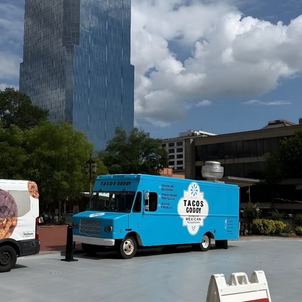 A bright blue Tacos Godoy food truck parked outdoors with a modern glass building in the background.